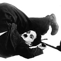 The silent-film comedian Charlie Chaplin, a master of visual humor, poses in character as “the Little Tramp.”