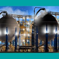 Photo illustration of large spherical liquefied natural gas (LNG) storage tanks at an industrial facility, with surrounding pipes, scaffolding, and vapor emissions under a blue sky.