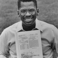 Lonnie Johnson, inventor of Super Soaker, a large plastic pump-action water gun, holding U.S. patent for his invention while sitting on grass outside his home.