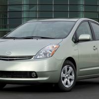 A 2006 silver Toyota Prius hybrid hatchback parked in front of a modern glass building, viewed from the front-left angle.