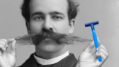 A black-and-white photo of a white man from the late 19th century wearing an extremely long mustache. Cut-out hands hold a blue razor to the right side of the image.