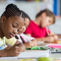A young female student writing in a notebook at her desk at school.